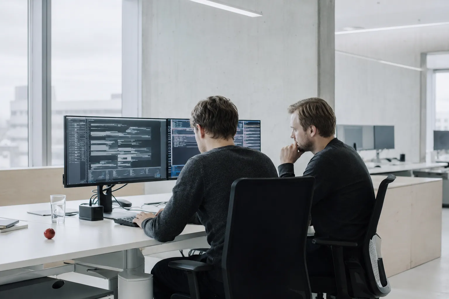 Two software engineers at a two-monitor desk.
