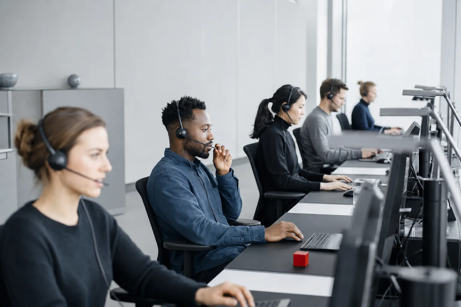 A row of professionals with headsets at well-spaced workstations.